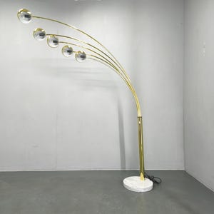 May include: A gold-toned arc floor lamp with five clear globe lights. The lamp has a white marble base and a curved design. The lamp is a modern lighting fixture.