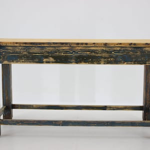 Puede incluir: Una mesa de madera rústica con un acabado de pintura azul desgastada. La mesa tiene un diseño sencillo con cuatro patas y un solo estante. La parte superior de la mesa está hecha de madera natural de color marrón claro.
