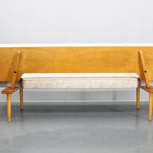 May include: A light wood frame sofa with a light gray fabric cushion. The sofa has a simple design with four legs and a back that folds down.