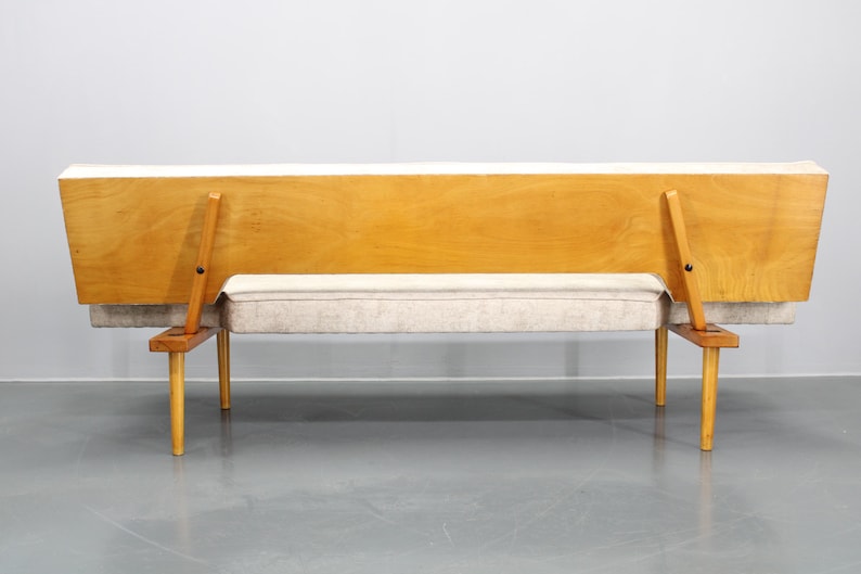 May include: A light wood frame sofa with a light gray fabric cushion. The sofa has a simple design with four legs and a back that folds down.