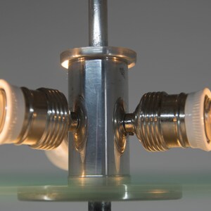 May include: Close-up of a silver metal lamp base with three light bulb sockets and clear glass bulbs. The base has a hexagonal shape and is attached to a clear glass surface.