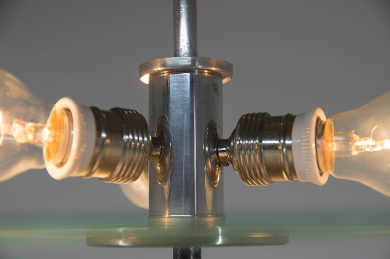 May include: Close-up of a silver metal lamp base with three light bulb sockets and clear glass bulbs. The base has a hexagonal shape and is attached to a clear glass surface.