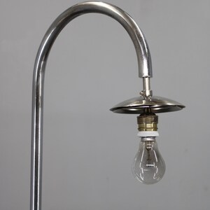 May include: A chrome-finished, arched floor lamp with a small, circular shade and a clear light bulb. The lamp has a minimalist design and a vintage aesthetic, suitable for home decor.