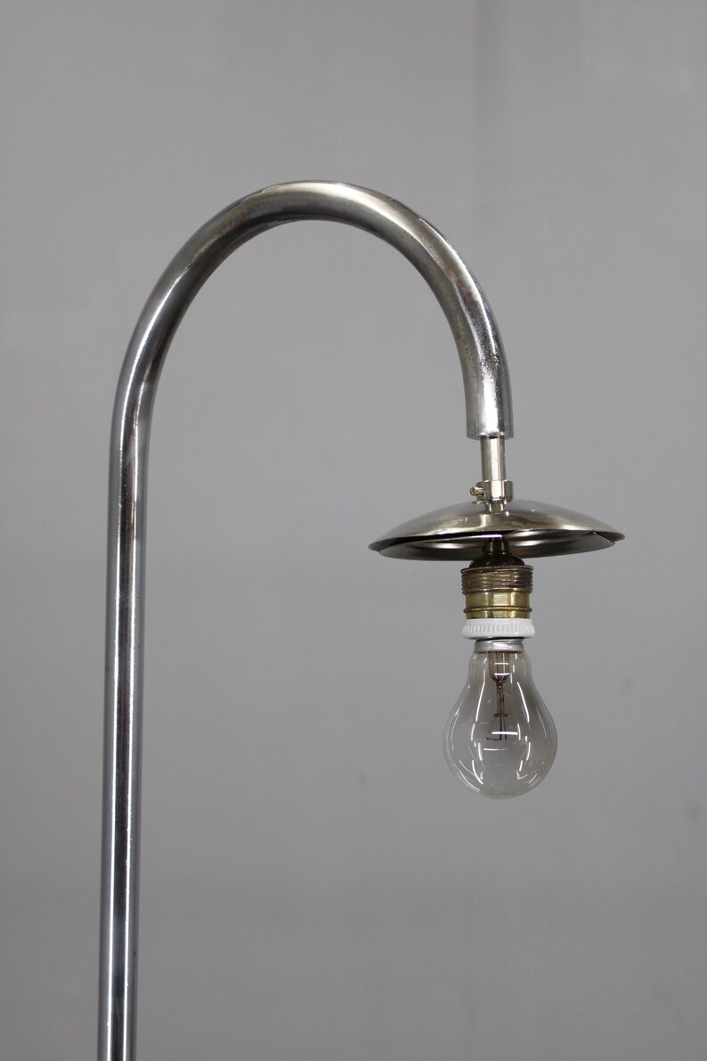 May include: A chrome-finished, arched floor lamp with a small, circular shade and a clear light bulb. The lamp has a minimalist design and a vintage aesthetic, suitable for home decor.
