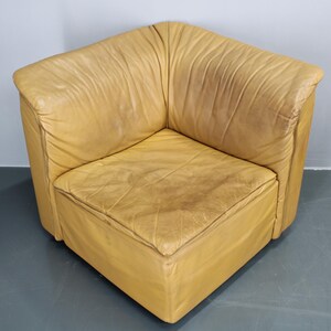 May include: A tan leather corner chair with a square seat and a slightly distressed look.