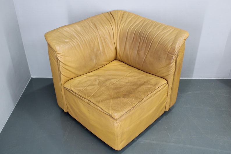 May include: A tan leather corner chair with a square seat and a slightly distressed look.