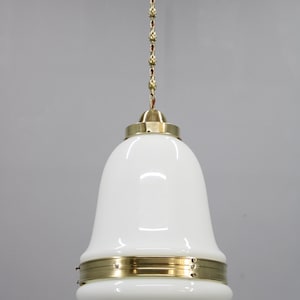 Op de afbeelding: Een witte glazen hanglamp met messing accenten. De lamp heeft een klokvormige kap en wordt opgehangen aan een decoratieve ketting. De messing details omvatten een ring rond de kap en een kap aan de bovenkant.