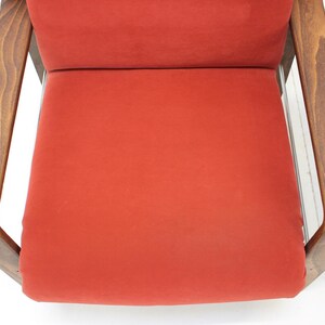May include: Close-up of a mid-century modern chair with a vibrant red seat and backrest. The chair features a wooden frame with a warm, natural finish. The design is simple and elegant, showcasing clean lines.