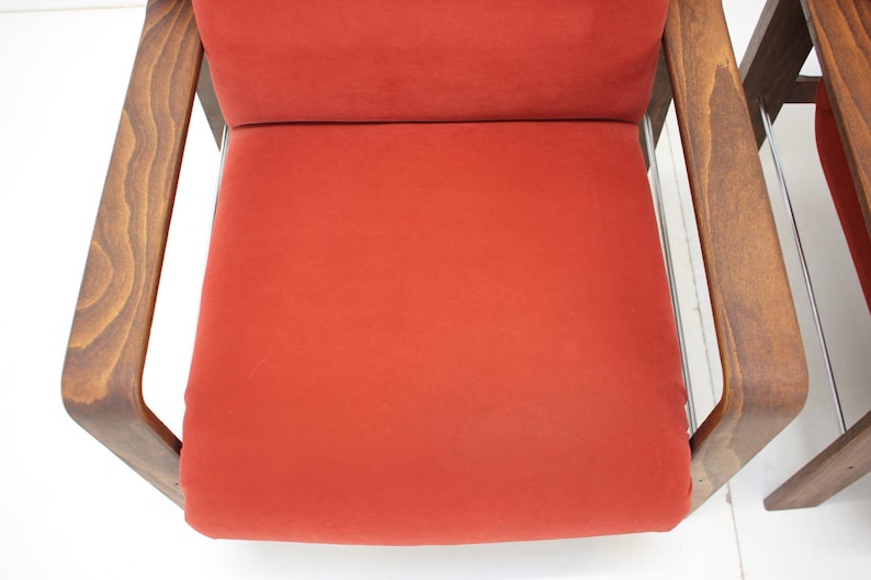 May include: Close-up of a mid-century modern chair with a vibrant red seat and backrest. The chair features a wooden frame with a warm, natural finish. The design is simple and elegant, showcasing clean lines.