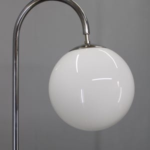 May include: A modern floor lamp with a chrome finish. The lamp features a curved arm supporting a large, white, globe-shaped light fixture. The lamp's design is minimalist and sleek, suitable for contemporary interiors.