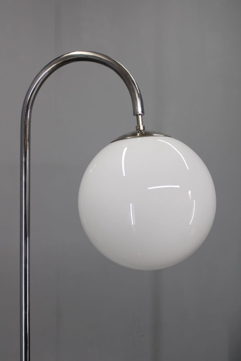 May include: A modern floor lamp with a chrome finish. The lamp features a curved arm supporting a large, white, globe-shaped light fixture. The lamp's design is minimalist and sleek, suitable for contemporary interiors.
