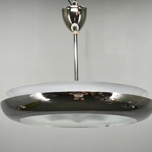 May include: A ceiling pendant light fixture featuring a polished chrome finish. The design includes a central vertical rod connected to a dome-shaped canopy, supporting a wide, circular, reflective chrome shade with a frosted glass diffuser.