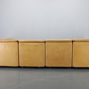 May include: A four-piece modular sofa with a light brown leather upholstery. The sofa is made up of four individual sections that can be arranged in different configurations.