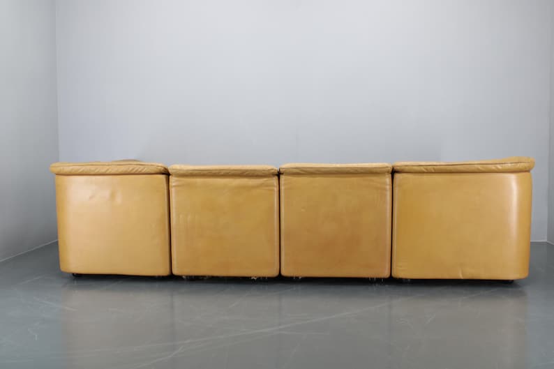 May include: A four-piece modular sofa with a light brown leather upholstery. The sofa is made up of four individual sections that can be arranged in different configurations.