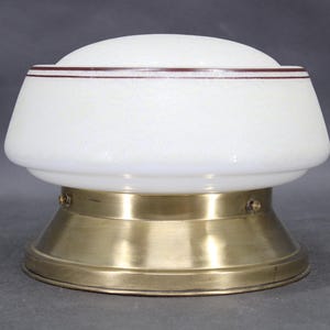 Könnte beinhalten: Eine Vintage-Leuchte mit weißem Glasschirm und Messingfuß. Der Schirm hat eine strukturierte Oberfläche und eine dunkelbraune Umrandung. Der Messingfuß hat eine konische Form. Diese antike Lampe eignet sich für die Inneneinrichtung.