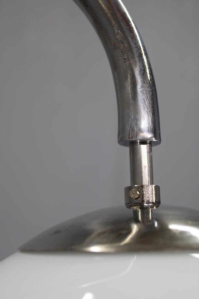 May include: Close-up of a modern lamp with a curved, brushed metal arm. The lamp features a white, rounded shade and a polished metal base. The design is minimalist and sleek, suitable for contemporary interiors.