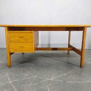 Könnte beinhalten: Ein hellbrauner Holzschreibtisch mit zwei Schubladen auf der linken Seite. Der Schreibtisch hat eine rechteckige Oberseite und vier Beine. Der Schreibtisch ist aus Holz und hat eine natürliche Oberfläche. Der Schreibtisch ist im Mid-Century-Modern-Stil gehalten.