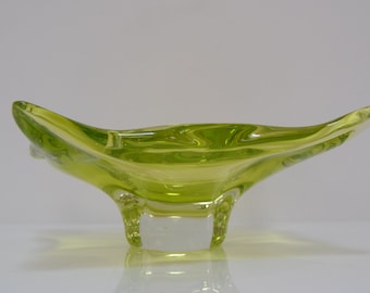 Puede incluir: Un cuenco de vidrio verde brillante con un diseño asimétrico único. El cuenco tiene una base ancha y poco profunda y un labio estrecho y puntiagudo. El cuenco está hecho de vidrio transparente con un tinte verde.