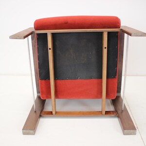 May include: A mid-century modern armchair with a red velvet seat and back. The chair has a wooden frame with a dark finish and clear acrylic side supports. The back of the chair is black.