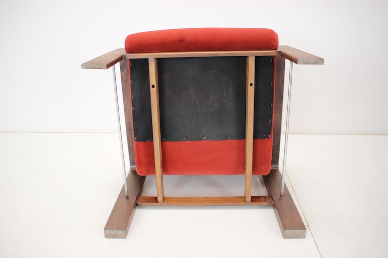 May include: A mid-century modern armchair with a red velvet seat and back. The chair has a wooden frame with a dark finish and clear acrylic side supports. The back of the chair is black.