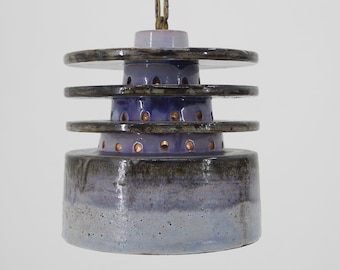 May include: A ceramic pendant light fixture with a layered design. The light has a purple and gray glaze with a textured finish. The light is suspended from a brass chain.