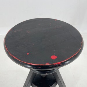 May include: Black wooden stool with a round seat and three legs. The seat has red paint accents.