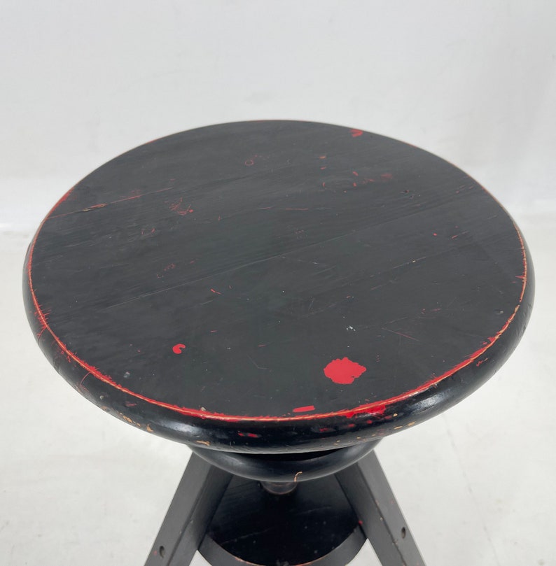 May include: Black wooden stool with a round seat and three legs. The seat has red paint accents.