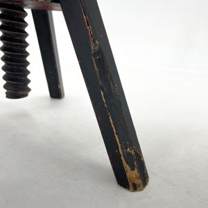May include: A wooden tripod stand with a black and red paint finish. The stand has a large, wooden screw in the center.