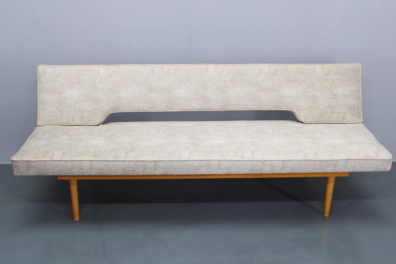 May include: A light gray fabric sofa bed with wooden legs. The sofa bed has a simple design and is in good condition.