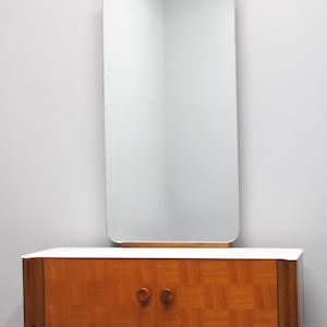 May include: A vintage wooden vanity with two doors and a large rectangular mirror. The vanity has a light wood finish with a geometric pattern and rounded edges. The mirror is framed in wood and has a beveled edge.