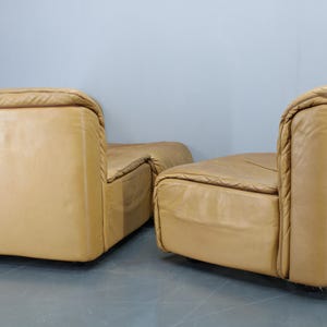 May include: Two tan leather chairs with a tufted design. The chairs are positioned side by side, with the back of each chair facing the camera.