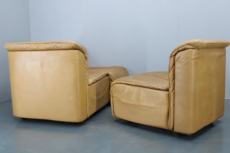 May include: Two tan leather chairs with a tufted design. The chairs are positioned side by side, with the back of each chair facing the camera.