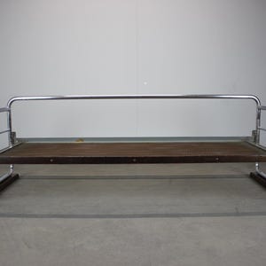 May include: A mid-century modern bench with a chrome frame and a woven brown seat. The bench has curved armrests and a rectangular wooden base. The design is minimalist and functional, suitable for a living room or entryway.