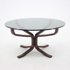 Peut inclure: Une table basse ronde avec un plateau en verre gris foncé et une base en bois brun foncé. La base a un design incurvé unique avec quatre pieds. La table mesure environ 76 cm de diamètre.