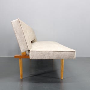 May include: A light beige fabric sofa with wooden legs. The sofa is a convertible sofa bed.