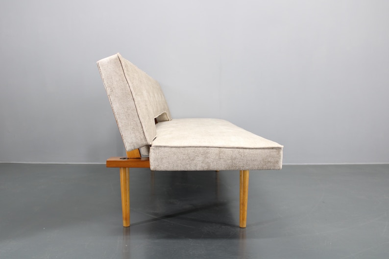 May include: A light beige fabric sofa with wooden legs. The sofa is a convertible sofa bed.