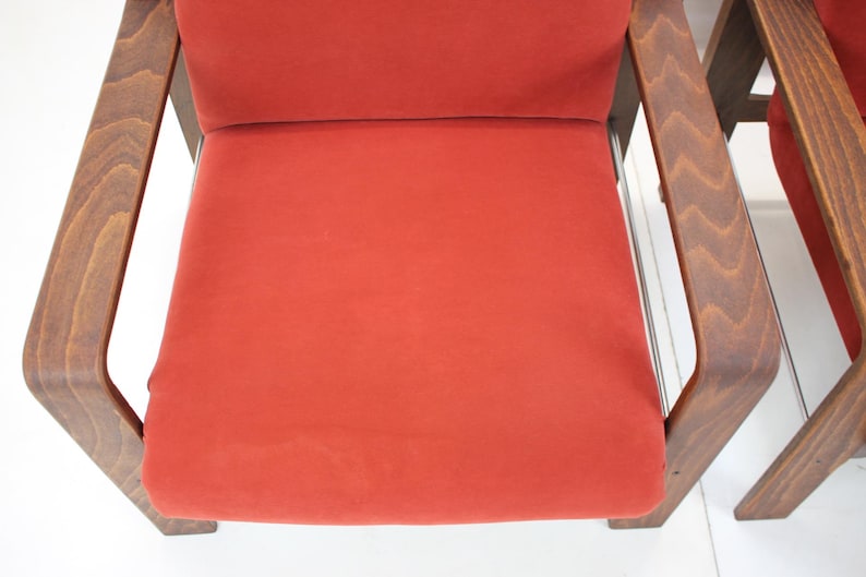 May include: Two mid-century modern chairs with a vibrant red seat and backrest. The wooden frames have a warm, brown finish. The chairs are set against a white background, highlighting their design.