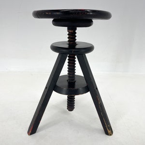 May include: A black wooden adjustable stool with a round seat and three legs. The stool has a screw mechanism to adjust the height.