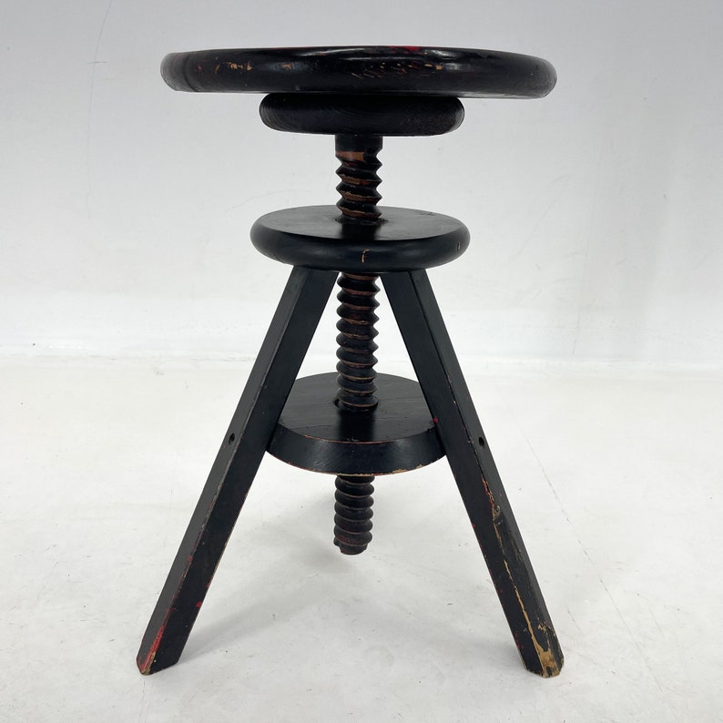 May include: A black wooden adjustable stool with a round seat and three legs. The stool has a screw mechanism to adjust the height.