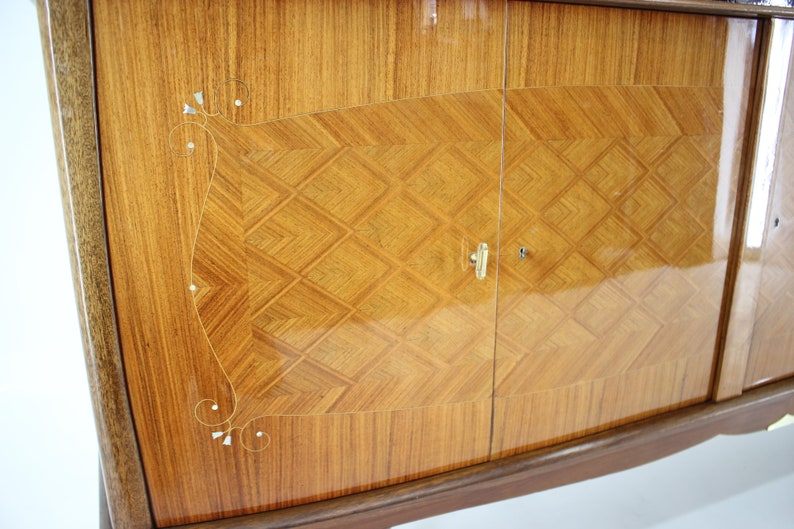 May include: A vintage wooden cabinet with two doors. The doors are made of wood with a diamond pattern and have a brass handle. The cabinet has a curved bottom and is decorated with a floral design.