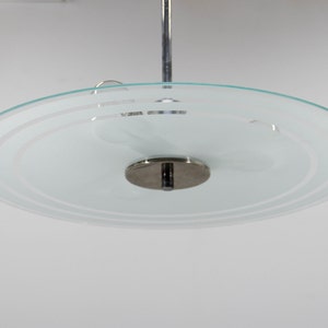 May include: A chrome and frosted glass ceiling light fixture with a circular design. The glass shade has a concentric circle pattern.