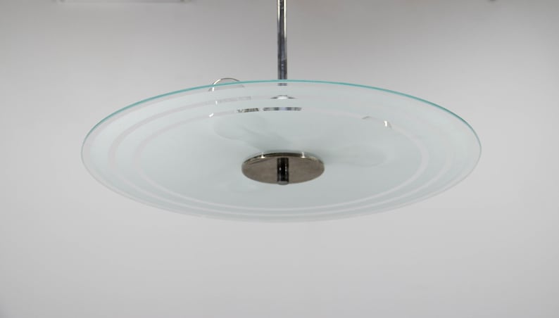 May include: A chrome and frosted glass ceiling light fixture with a circular design. The glass shade has a concentric circle pattern.