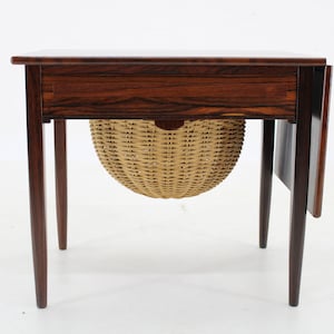 Pode incluir: Uma mesa de madeira escura com tampo dobrável e uma cesta de vime pendurada por baixo. A mesa tem uma única gaveta e um tampo dobrável no lado direito.