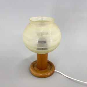 Puede incluir: Una l&aacute;mpara de mesa vintage con una pantalla de vidrio blanco texturizada y una base de madera. La base tiene una plataforma redonda de madera.