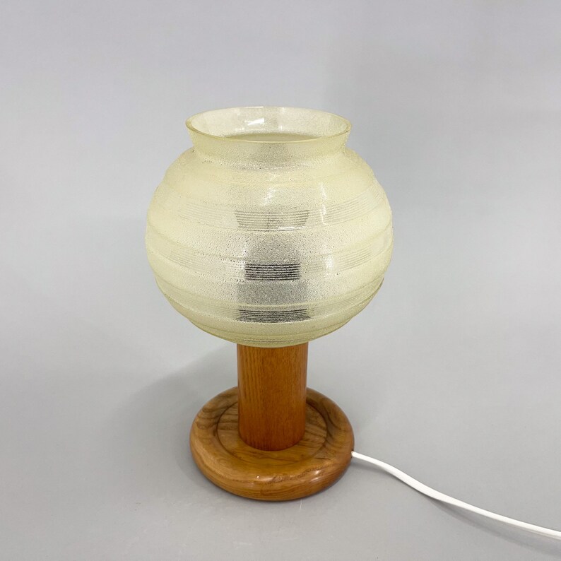 Puede incluir: Una l&aacute;mpara de mesa vintage con una pantalla de vidrio blanco texturizada y una base de madera. La base tiene una plataforma redonda de madera.