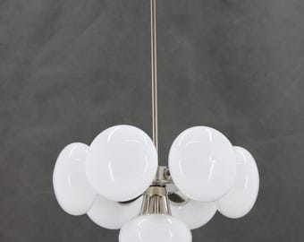 Könnte beinhalten: Ein Chrom-Kronleuchter mit sechs weißen Glaskugeln. Der Kronleuchter hat einen langen, dünnen Stiel und ein schlichtes, modernes Design.