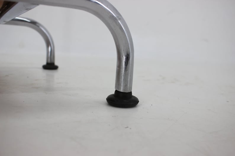 May include: Close-up of the chrome legs of a chair with black rubber feet.