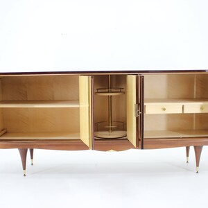 May include: A mid-century modern wooden cabinet with four doors, two shelves, and two drawers. The cabinet is made of dark wood with a light wood interior. The doors are open, revealing the interior.