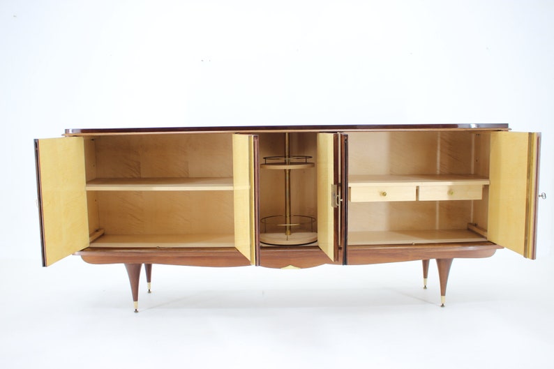May include: A mid-century modern wooden cabinet with four doors, two shelves, and two drawers. The cabinet is made of dark wood with a light wood interior. The doors are open, revealing the interior.