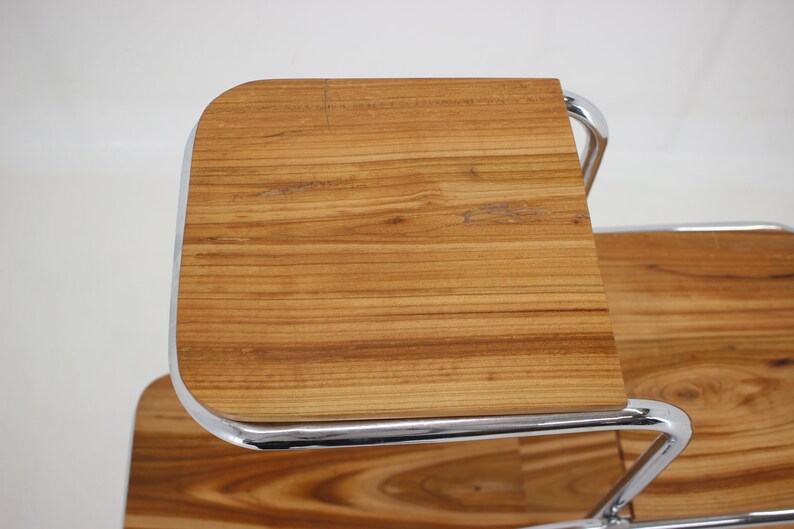 May include: A chrome and wood serving cart with two tiers. The top tier is made of wood with a natural finish and has a rounded edge. The bottom tier is also made of wood with a natural finish.